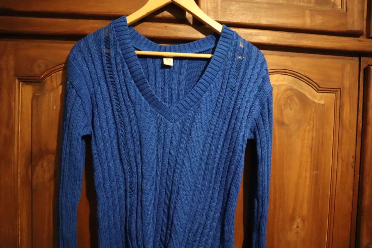 Sweater azul de tejido con cuello en V y detalles de ochos en el frente. Posee mangas largas y un calado sutil en los hombros.