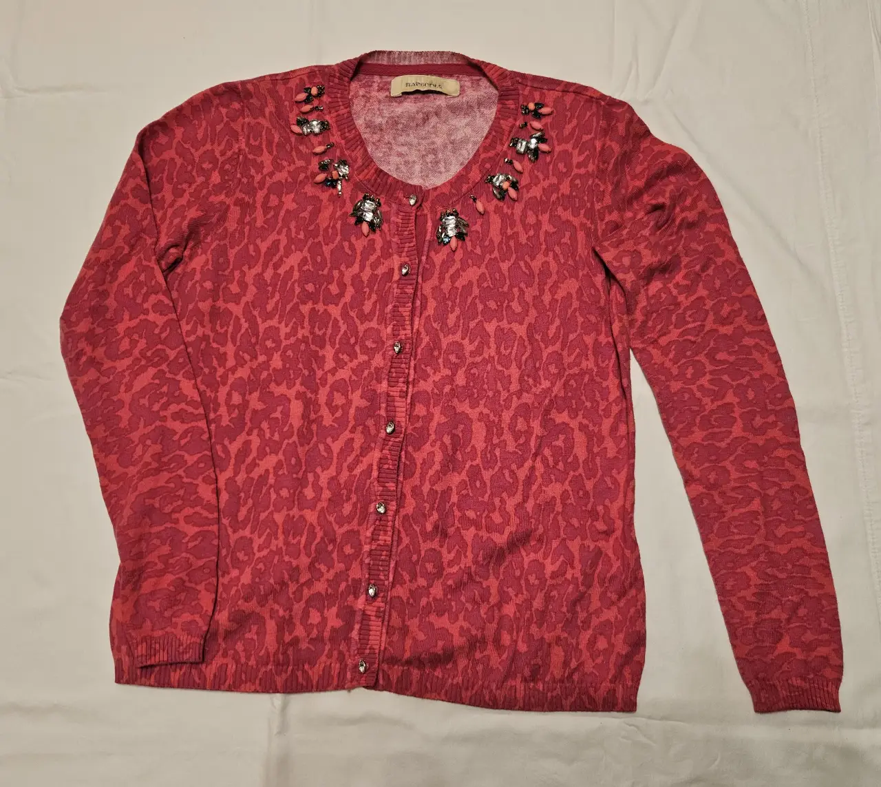 Cardigan de mujer en tono fucsia con estampado de leopardo. Detalles de pedrería en el cuello y botones decorativos. Ideal para un look elegante y sofisticado.