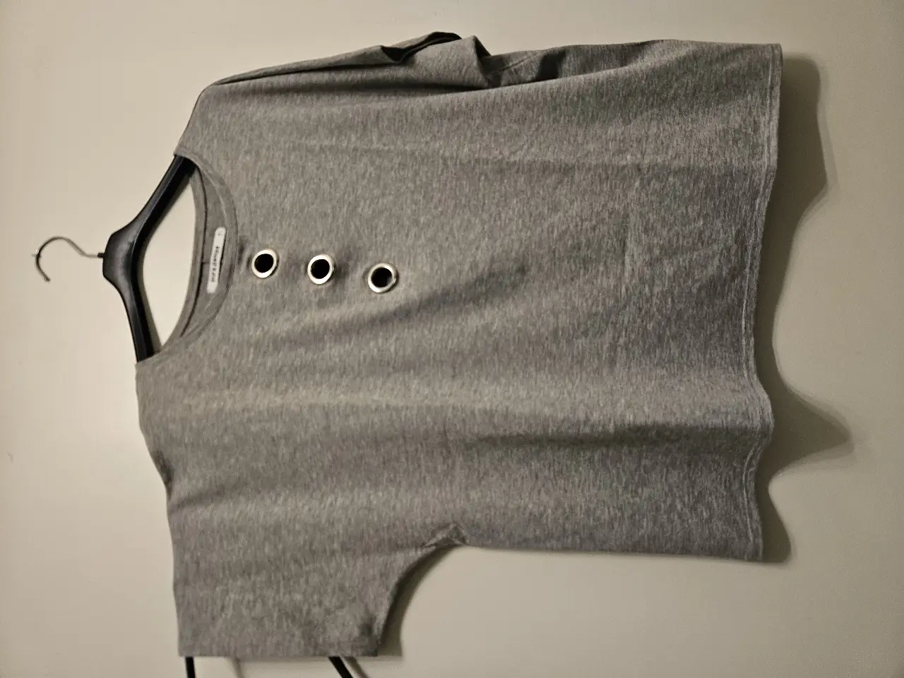 Remera gris de manga corta con detalles de ojales metálicos en el frente. Ideal para un look casual y moderno.