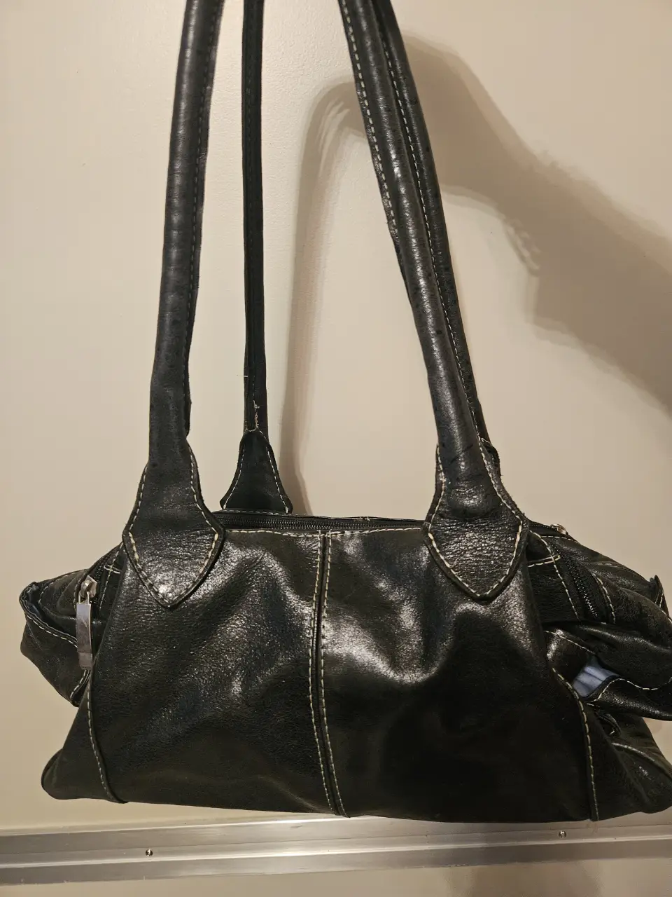 Cartera negra de cuero con costuras blancas. Ideal para llevar al hombro, con un diseño elegante y versátil. Bolsillos internos y externos