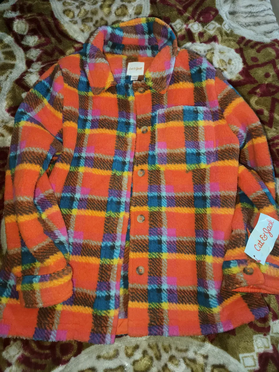 Campera de abrigo a cuadros en tonos naranja, azul, rosa y marrón. Posee botones al frente y bolsillos.