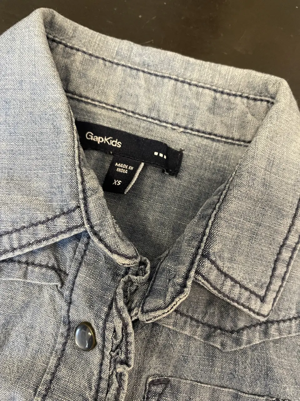 Camisa de jean GapKids, celeste, talle XS, con detalles de costuras en contraste y botones. Ideal para un look casual y moderno.