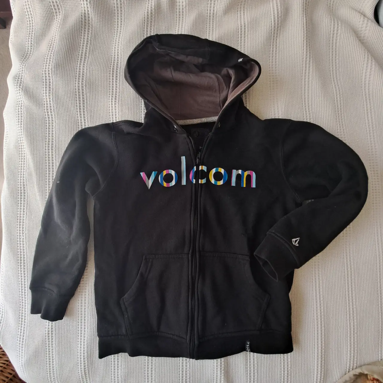 Buzo con cierre Volcom negro para niño, con logo multicolor en el frente y detalle de la marca en la manga. Ideal para un look casual y abrigado.