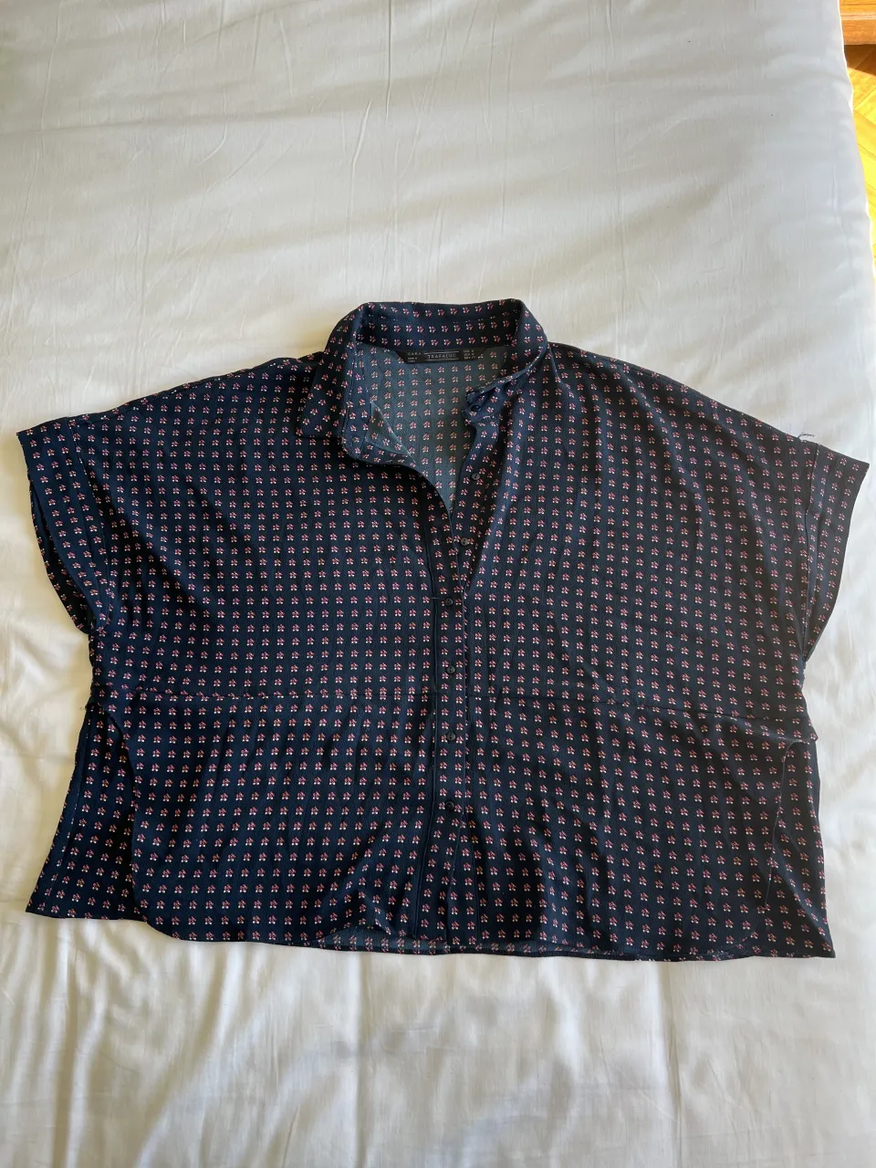 Camisa estampada con flores pequeñas en tonos azul y rosa. Posee cuello camisero y botones al frente. Ideal para un look casual y fresco.