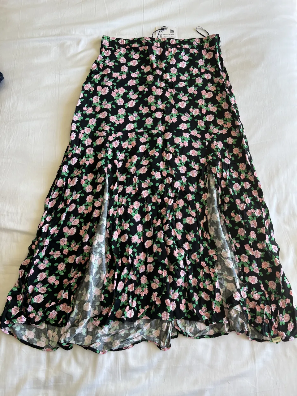 Pollera larga estampada con flores rosas sobre fondo negro. Posee dos tajos amplios en el frente que le dan movimiento. Ideal para un look fresco y femenino.