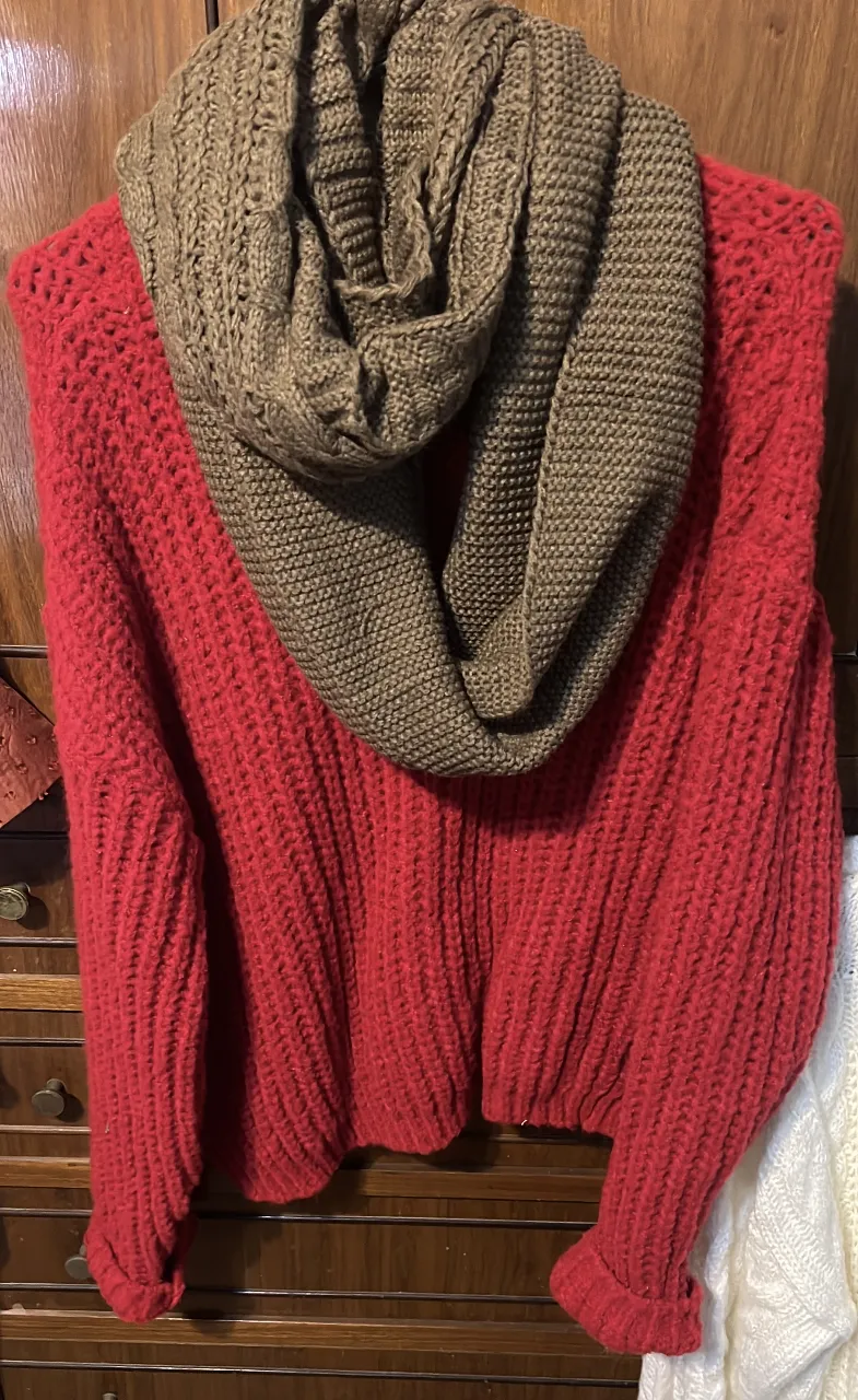 Sweater rojo tejido con cuello redondo y mangas largas. Incluye un cuello bufanda marrón tejido. Ideal para un look casual y abrigado.