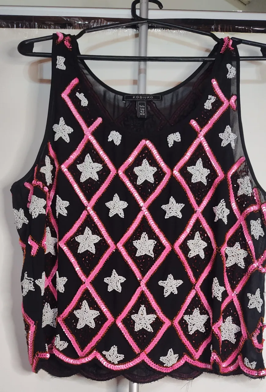 Kosiuko Musculosa corta de gasa negra con un bordado integral de lentejuelas en colores fucsia y plateado, formando un patrón de rombos con estrellas blancas en su interior. negro con canutillos y lentejuelas rosas y blancas en forma de estrellas y rombos. Ideal para una salida nocturna o una fiesta.