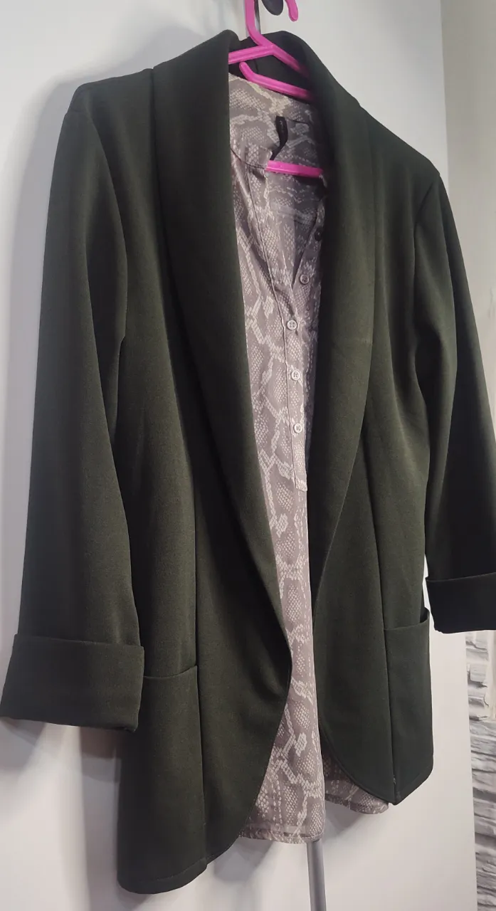 Blazer práctico para media estación verde oscuro con solapas anchas y mangas tres cuartos con puños doblados. La camisa que se ve debajo es estampada con un patrón de escamas en tonos grises y blancos. de sisa a sisa 45 cm  de hombro 10 cm 