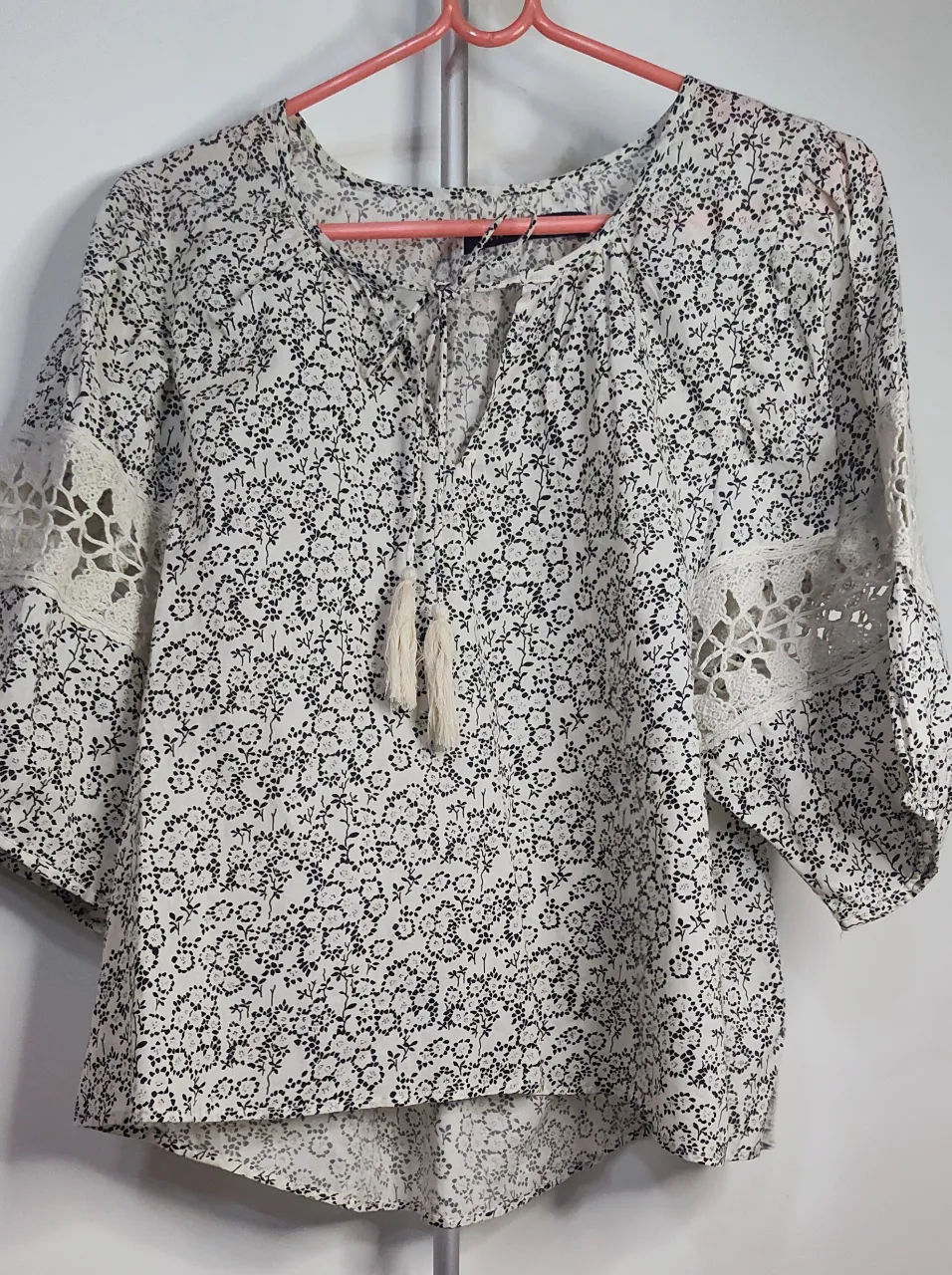 Blusa blanca estilo bohemio con estampa floral en negro. Posee mangas 3/4 con detalles de encaje y tiras con flecos en el escote.