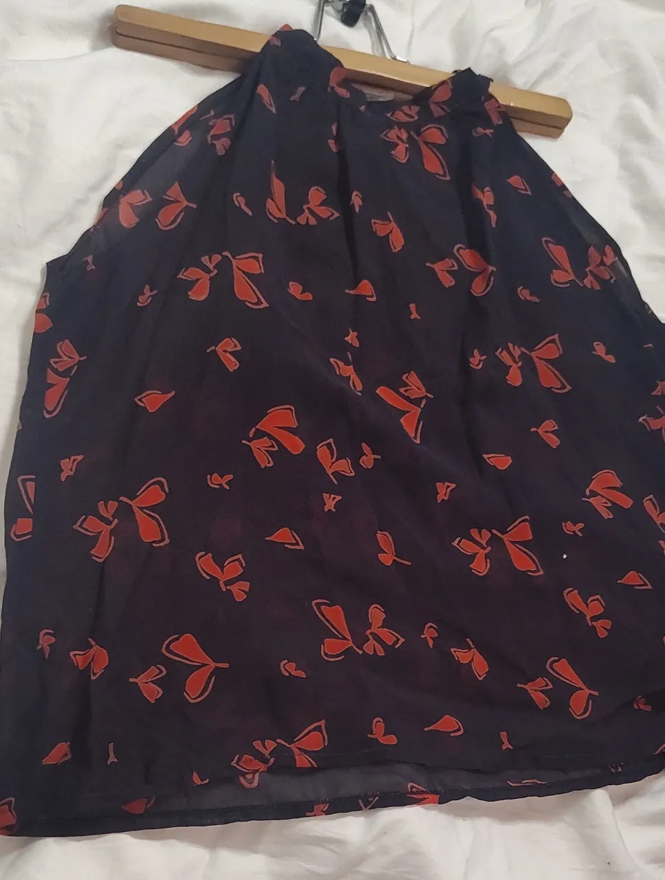 Esta blusa de color azul oscuro presenta un diseño de cuello tipo halter y un llamativo estampado de lazos en tonos rojizos El tejido  gasa  ligero y semitransparente, ideal para un look canchero y femenino. Perfecto para usar en salidas informales o para darle un toque especial a tu outfit.