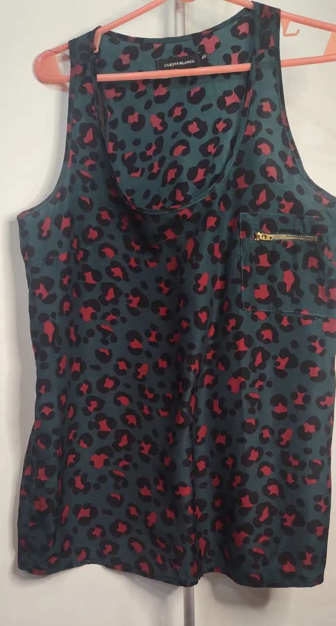 Hermosa realza tu aufiis, Musculosa presenta un llamativo estampado de leopardo en tonos rojos y negros sobre un fondo verde oscuro. Es una prenda de la marca Cuesta Blanca, diseñada sin mangas y con un bolsillo en el pecho que incluye un detalle de cierre metálico dorado.  de sisa a sisa 48.