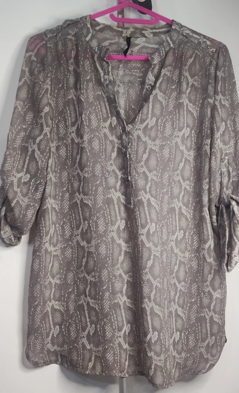 Blusa gris con estampa de serpiente en blanco y negro.  talle 38 de sisa a sisa 48 cm, estampado  de reptil, en tonos grises y blancos. estilo "Henley" Cuenta con un cuello mao " con una hilera de botones frontal, Tiene mangas 3/4 ajustables mediante una tira con botón (roll-tab) y un corte fluido con bajo redondeado.