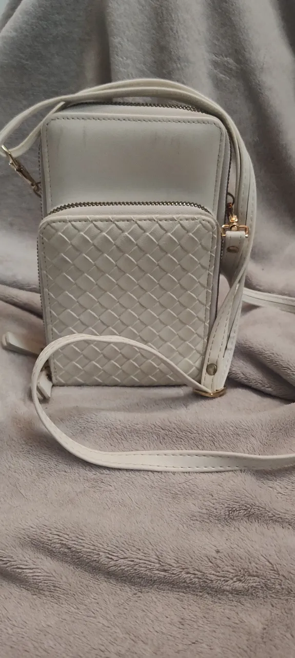 Cartera tipo bandolera de cuero sintético color blanco roto. Posee múltiples compartimentos con cierre y un bolsillo frontal con tejido texturizado. Correa larga ajustable.