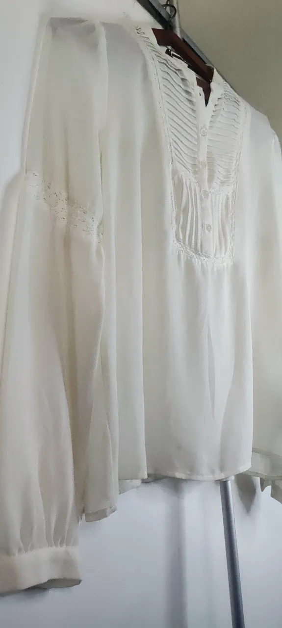 Esta blusa de color marfil presenta un diseño de inspiración bohemia con detalles de alforjas refinadas (finos pliegues cosidos) en el pecho y un delicado encaje que bordea el panel frontal y las mangas blanca, kv en Posee cuello mao y botones al frente. de sisa a sisa 46 cm 