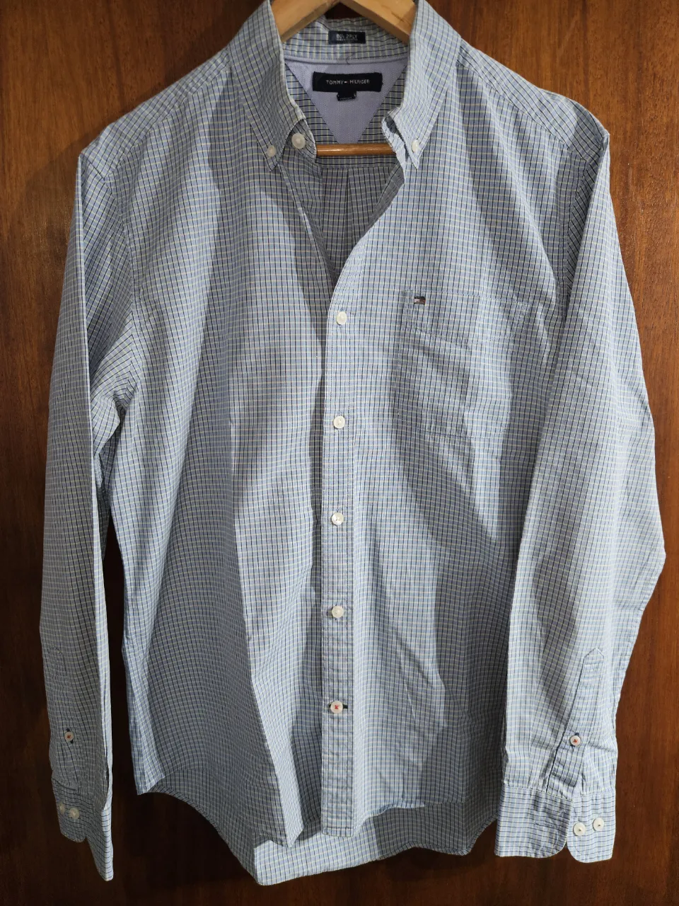 Camisa de vestir a cuadros celestes y blancos, con detalles en azul marino y amarillo. Posee botones blancos y un pequeño logo bordado en el pecho. Ideal para un look casual o de trabajo. Le falta un botón solamente (última foto)