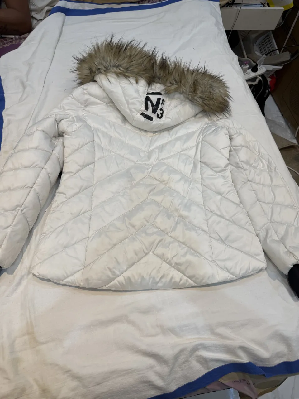 Campera blanca acolchada con capucha y detalles de piel sintética. Posee cierre frontal y bolsillos laterales con cierre.