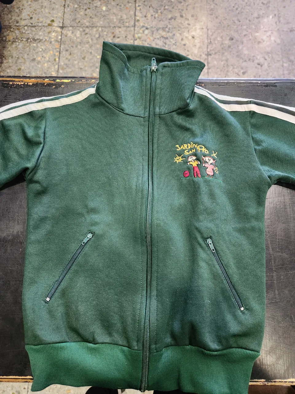 Buzo deportivo verde con cierre y detalles uniforme instituto San Pío + chomba de piqué ambos talle 2 años. Tiene un bordado en el pecho con un diseño del instituto. 