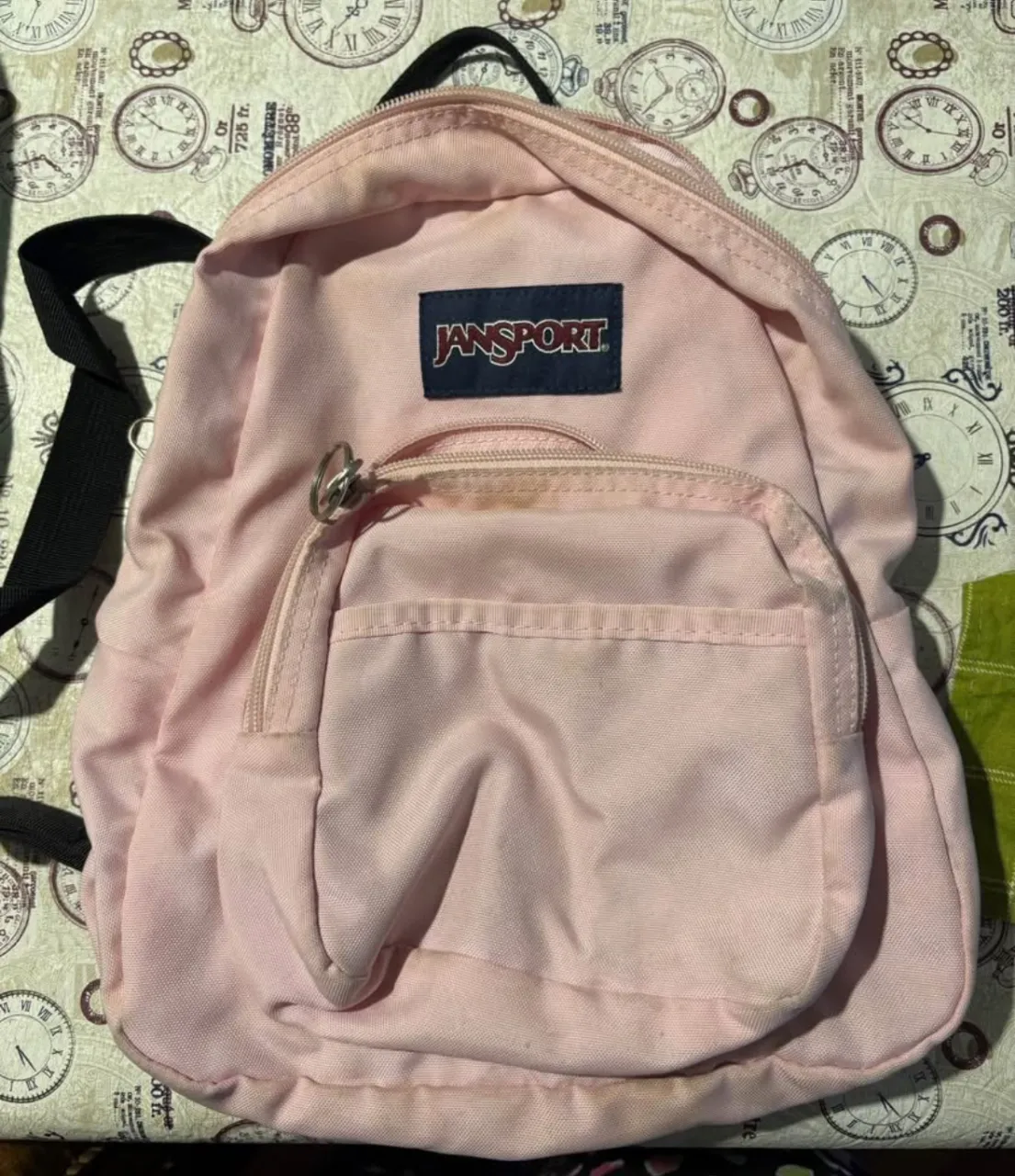 Mochila pequeña Jansport rosa, ideal para uso diario. Cuenta con un bolsillo frontal y un compartimento principal. Perfecta para llevar tus cosas con estilo.