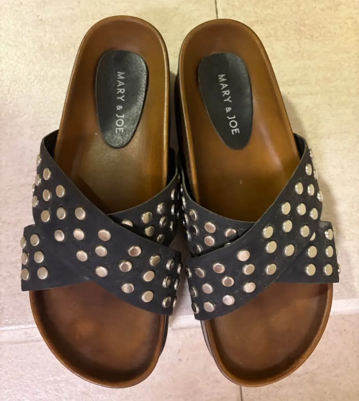 Sandalias de mujer MARY & JOE con diseño cruzado y tachas plateadas. Base de madera marrón.