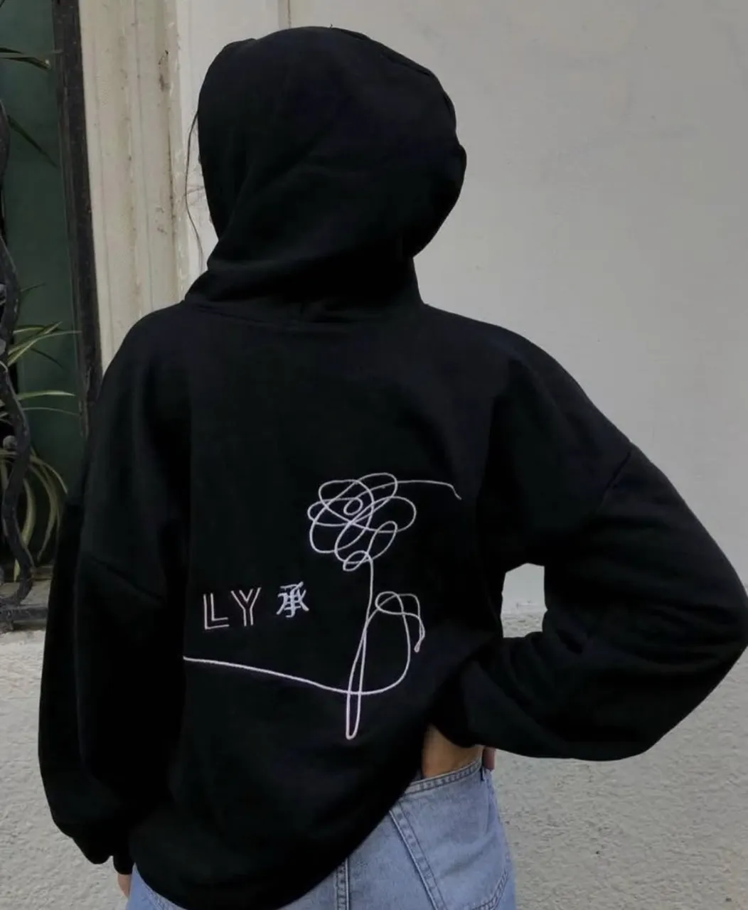 Buzo negro con capucha, estampado de flor blanca y logo de BTS en el frente. Ideal para fans de K-pop.