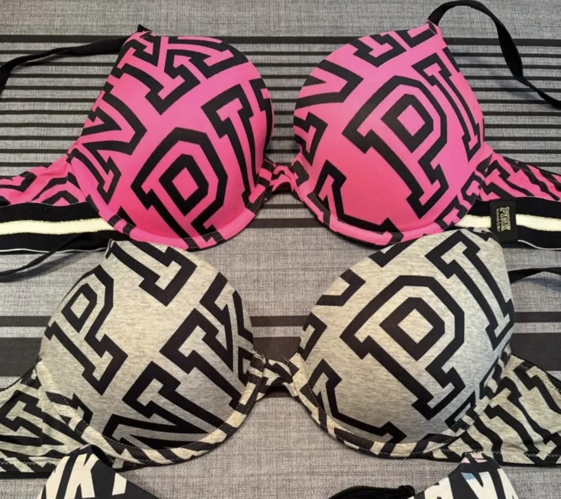 Conjunto de dos corpiños de la marca Pink, con estampa de letras en negro sobre fondo rosa y gris. Ideales para el uso diario o deportivo.