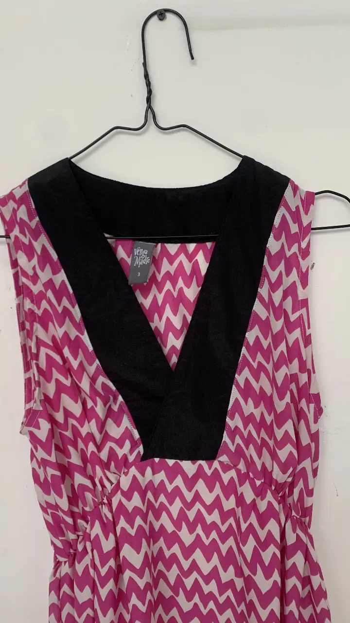 Vestido midi para embarazada. Corte irregular con estampado de zig-zag en tonos rosa y blanco. Tiene un escote en V con detalle negro y cintura marcada. Ideal para un look fresco y femenino.