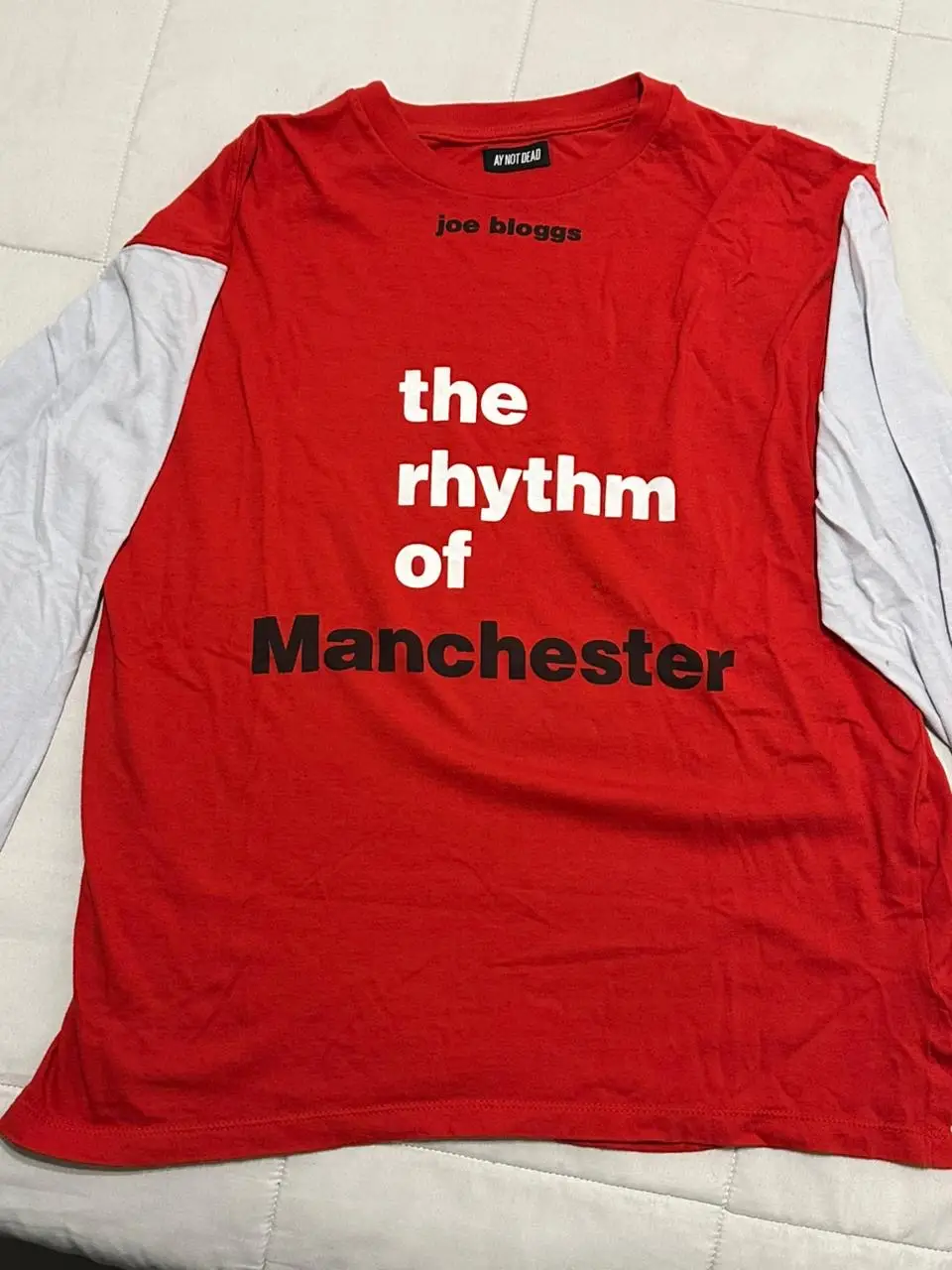 Remera manga larga roja con mangas blancas. Estampado "the rhythm of Manchester" en negro. Cuello redondo. Ideal para un look casual y urbano.