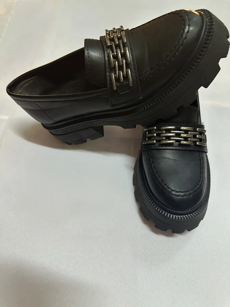 Mocasines negros con detalle de cadena plateada en la capellada y suela track.