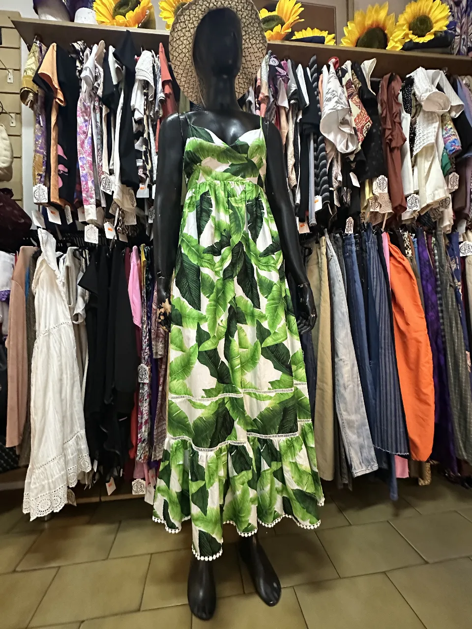 Vestido largo de verano con estampado de hojas verdes sobre fondo blanco. Tiene tirantes finos, escote en V y detalles de volantes con terminación de bolillos en el ruedo. Ideal para un look fresco y cómodo.