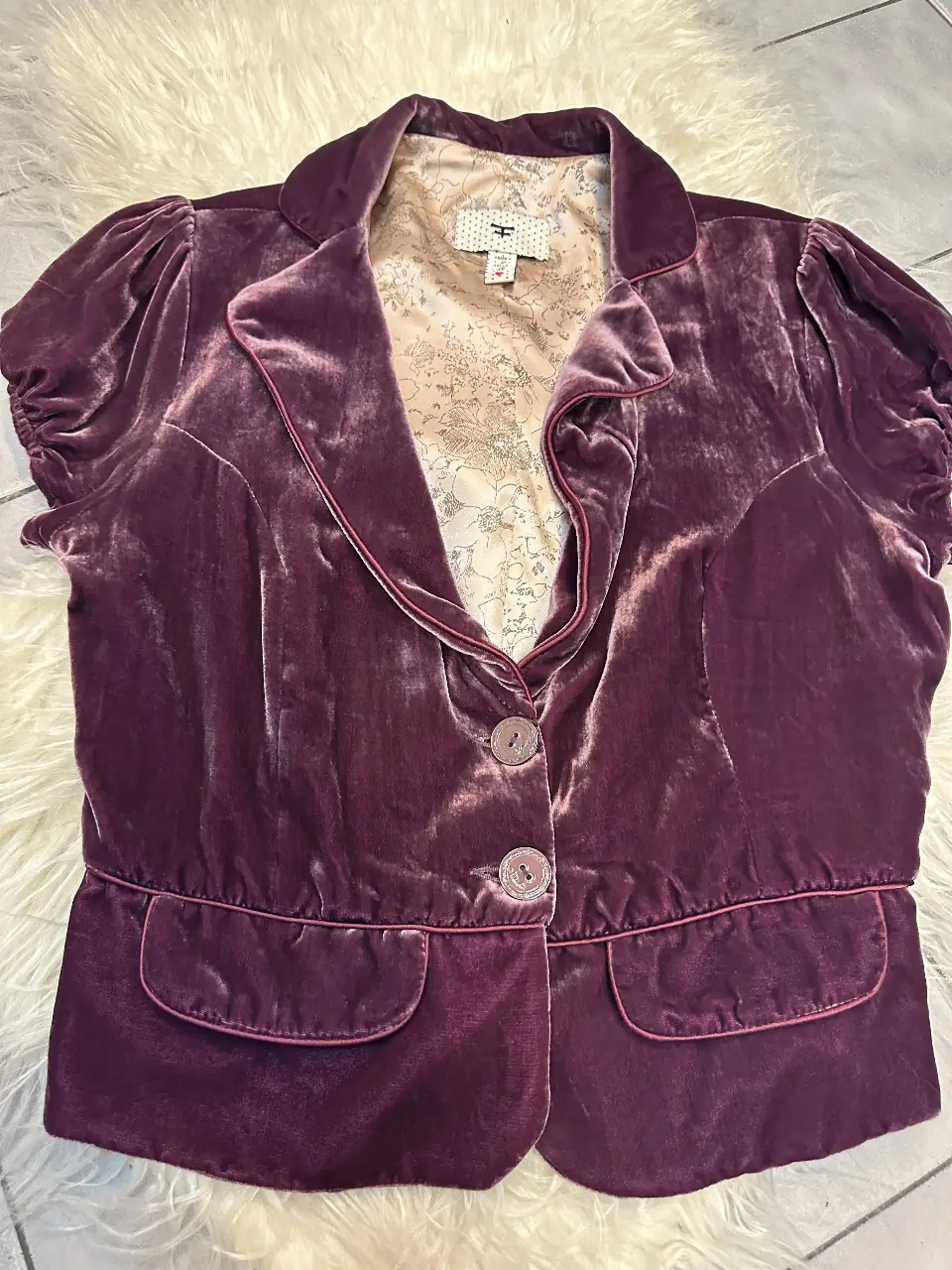 Blazer de terciopelo color violeta con mangas cortas abullonadas. Posee dos bolsillos delanteros y dos botones para cerrar. Ideal para un look elegante y sofisticado.