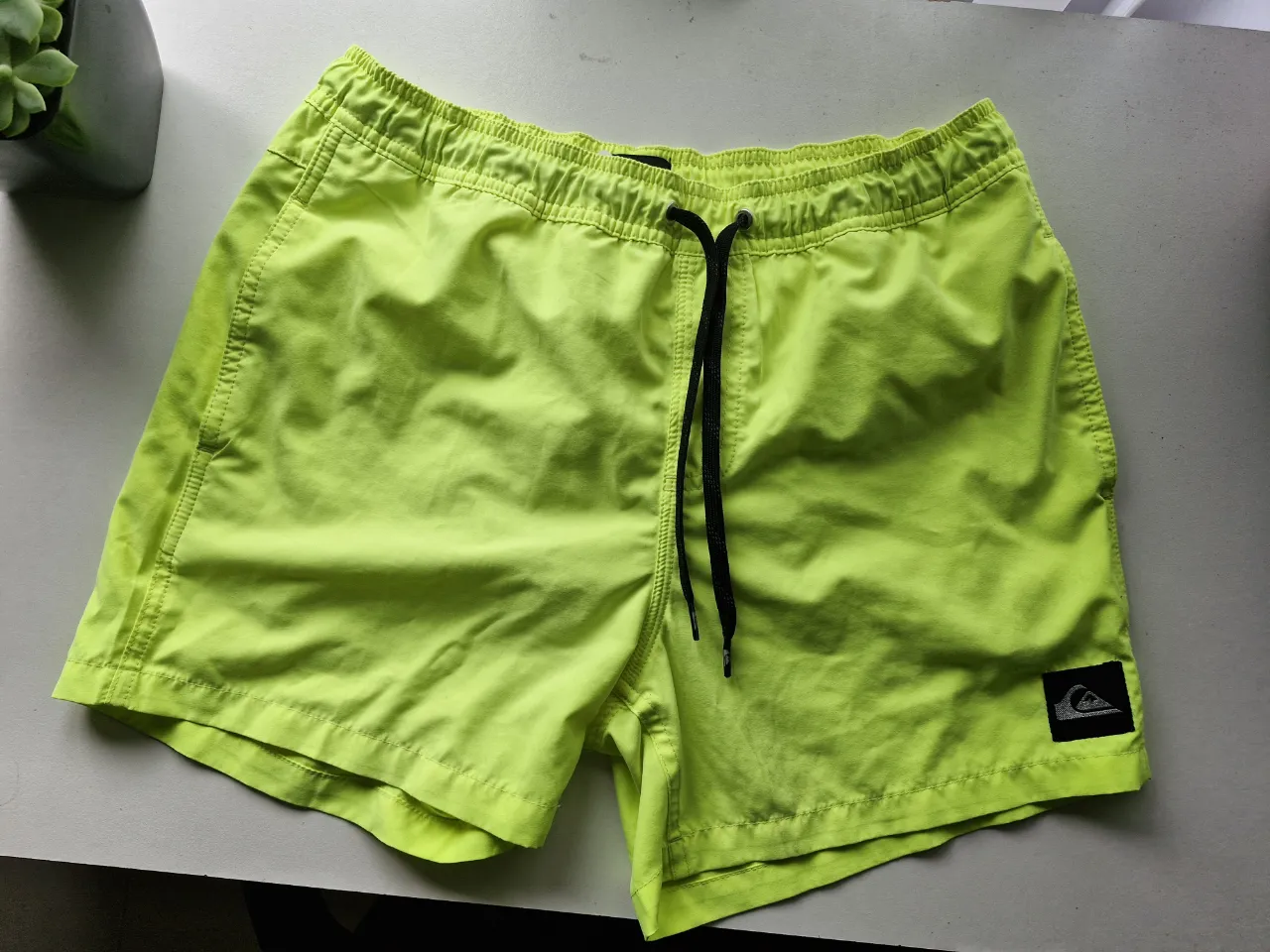 Shorts de baño color verde flúo con cordón negro para ajustar en la cintura. Posee un pequeño logo de la marca en la parte inferior izquierda.