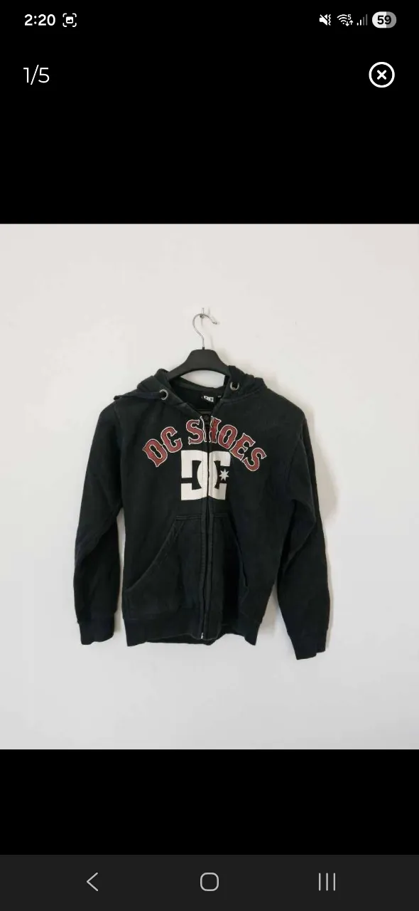 Buzo con capucha y cierre completo, de color negro. Presenta estampa de la marca 'DC Shoes' en el frente, con letras rojas y blancas.