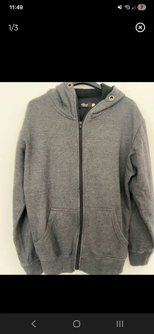 Buzo gris con capucha y cierre completo. Posee bolsillos frontales tipo canguro.