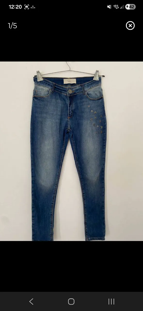 Jeans de corte ajustado con detalles de apliques metálicos en forma de flores en el frente y bordado floral en el bolsillo trasero. Cierre de botón y zíper.