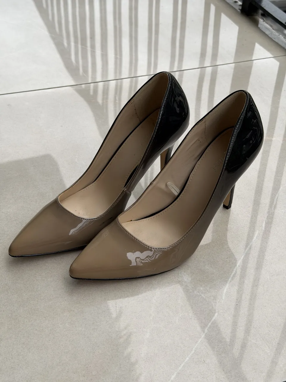 Zapatos de taco alto, estilo stiletto, con punta fina. Combinan un color nude en la parte delantera y un negro brillante en el talón y borde superior. Ideales para un look elegante y sofisticado. 26.5 cm de plantilla y 10cm de tacos 