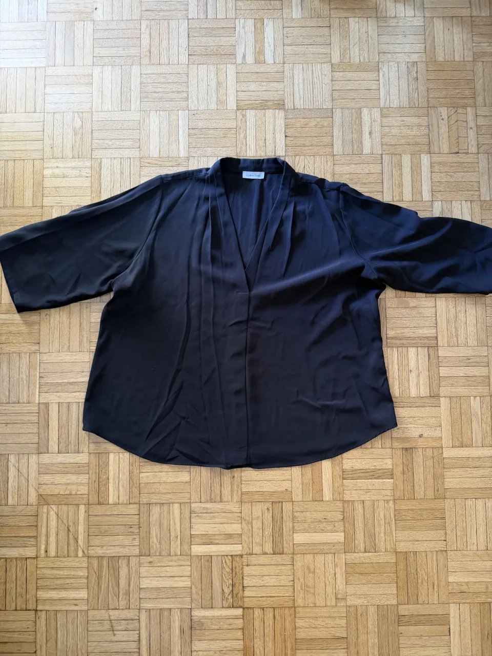 Blusa negra de manga 3/4 con cuello en V y detalles de pliegues en la parte delantera.