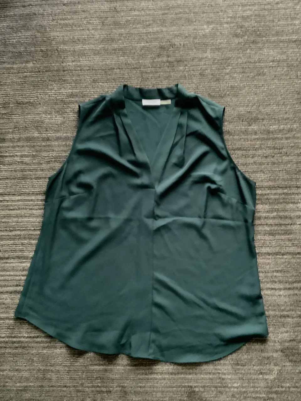 Musculosa verde oscuro con cuello en V y detalle de pliegues en el frente. Sin mangas.