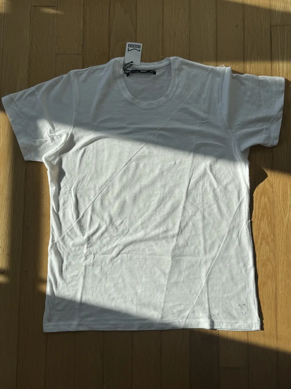Remera blanca de algodón MOCKBA, con un diseño diagonal sutil. Talle XXL, esta nueva con etiqueta pero posee un defecto en la parte derecha abajo. 