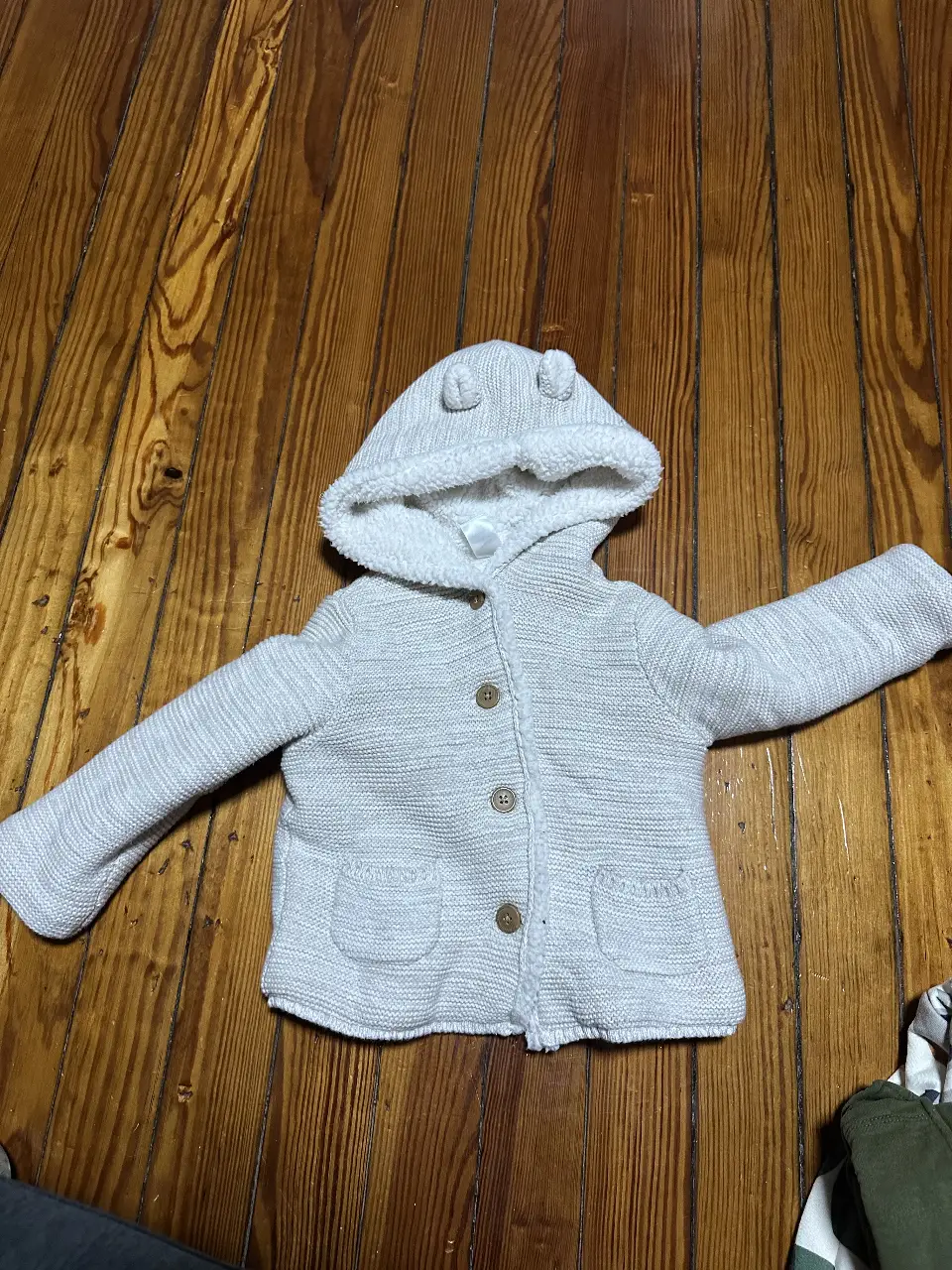 Cárdigan de bebé con capucha y orejas, color gris claro, con botones y bolsillos. Interior de sherpa blanco.