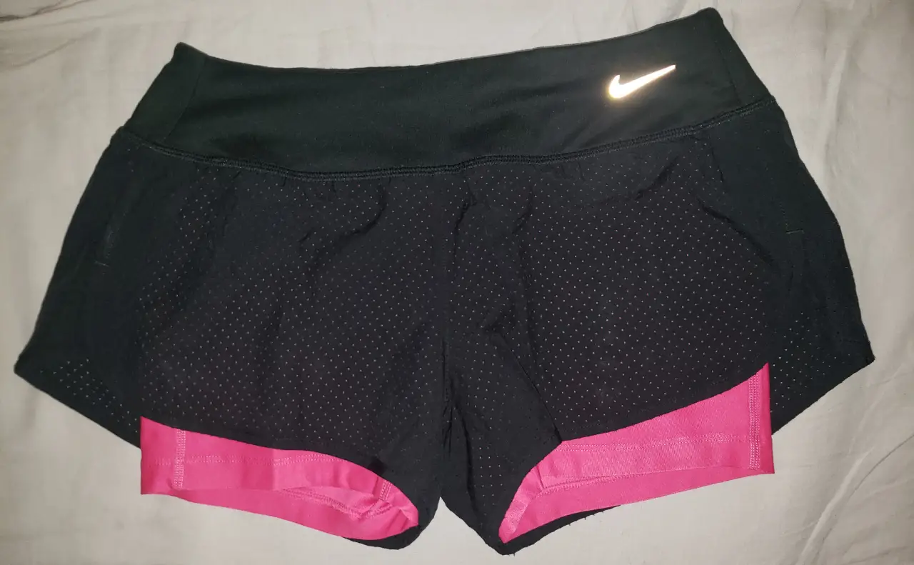 Short deportivo Nike de running para mujer, negro con interior rosa. Posee un bolsillo trasero con cierre y el logo de la marca en blanco reflectivo. Talle S.