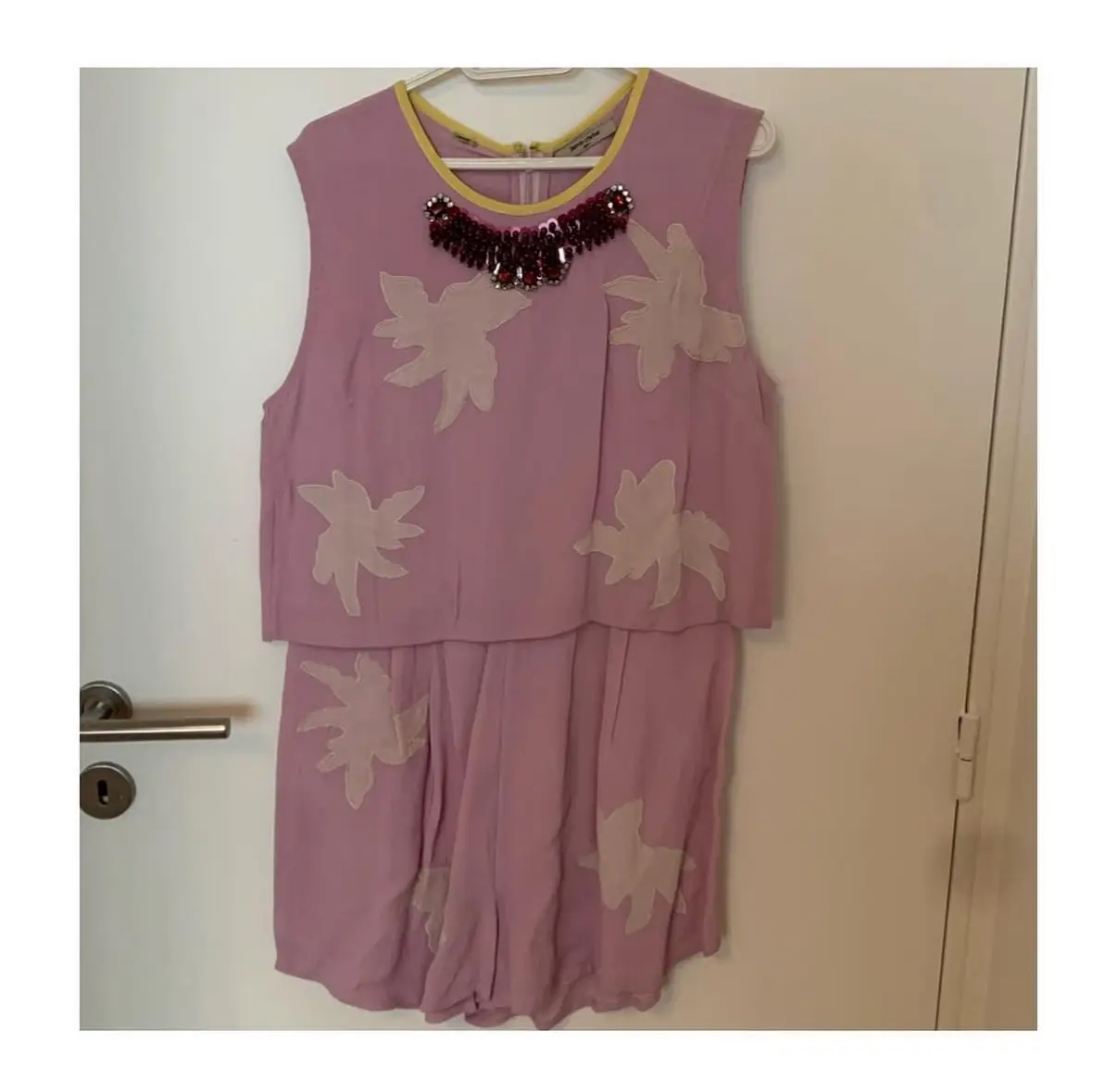 Mono corto de tela rosa con apliques florales en blanco. Cuello amarillo y detalle de piedras. Ideal para un look fresco y moderno.