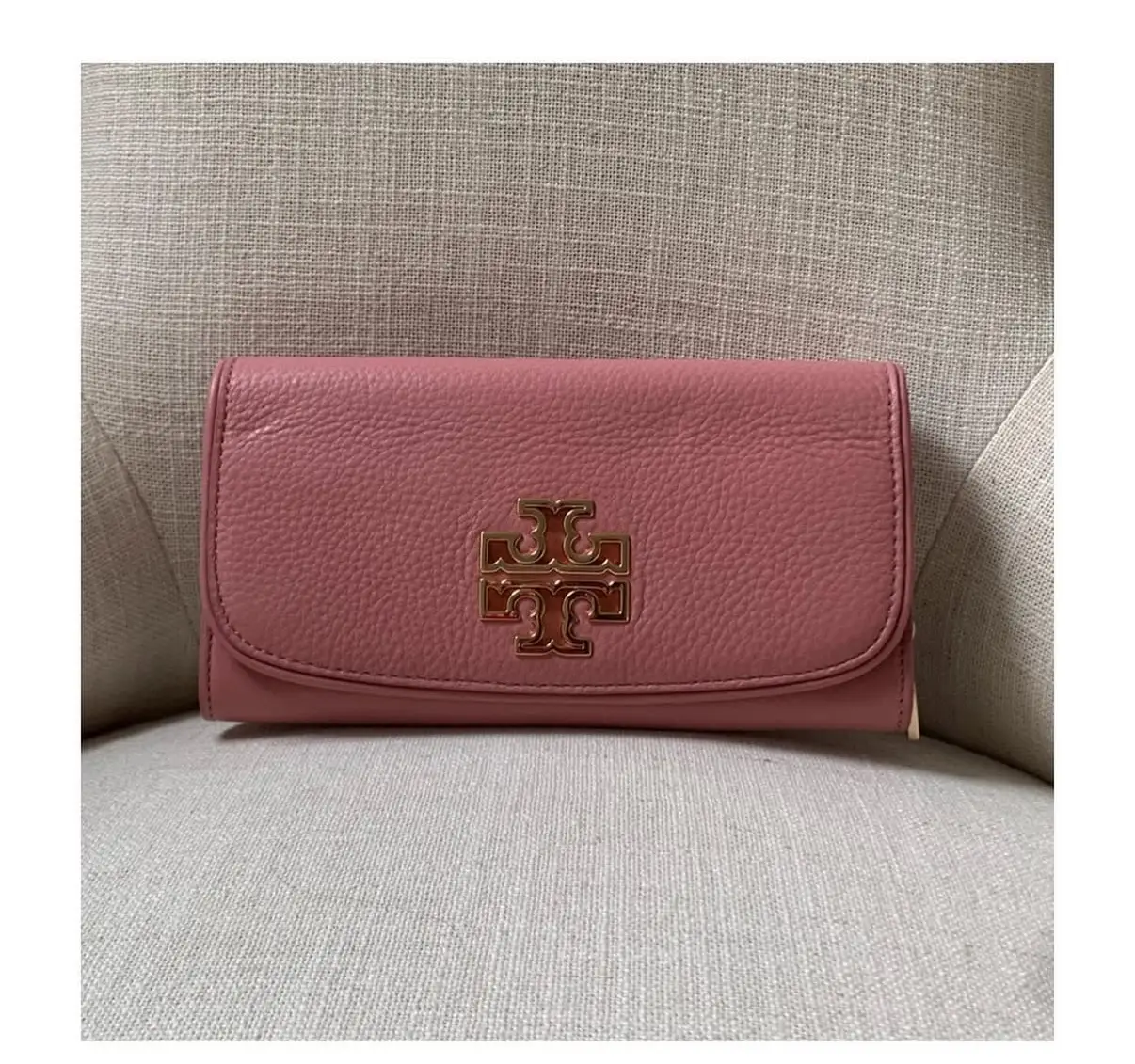Billetera de cuero rosa Tory Burch con el logo dorado en el frente. Diseño plegable con múltiples compartimentos para tarjetas y billetes. Un accesorio elegante y funcional para el día a día.