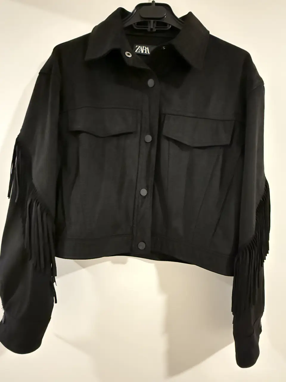 Campera negra de mujer estilo biker con flecos en las mangas y espalda. Marca Zara, talle S. Ideal para un look moderno y canchero.