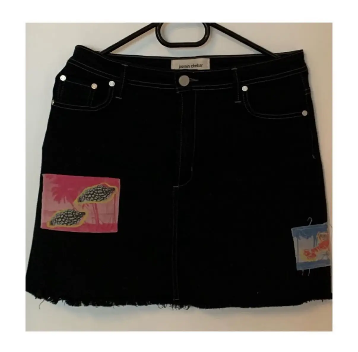 Minifalda de jean negra con parches estampados. Diseño con detalles de costura en blanco y borde desflecado. Ideal para un look casual y con onda.