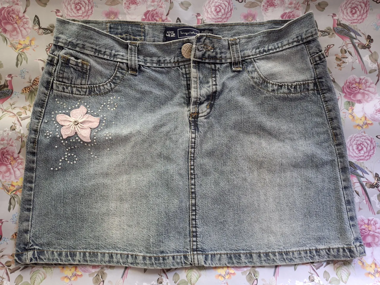 Mini de jean INQUIETA ,con detalles de flor y strass. Un clásico que nunca pasa de moda. Combinala con tus tops favoritos y zapatillas para un outfit perfecto. 
Largo       37 cm.
Cintura  43 cm