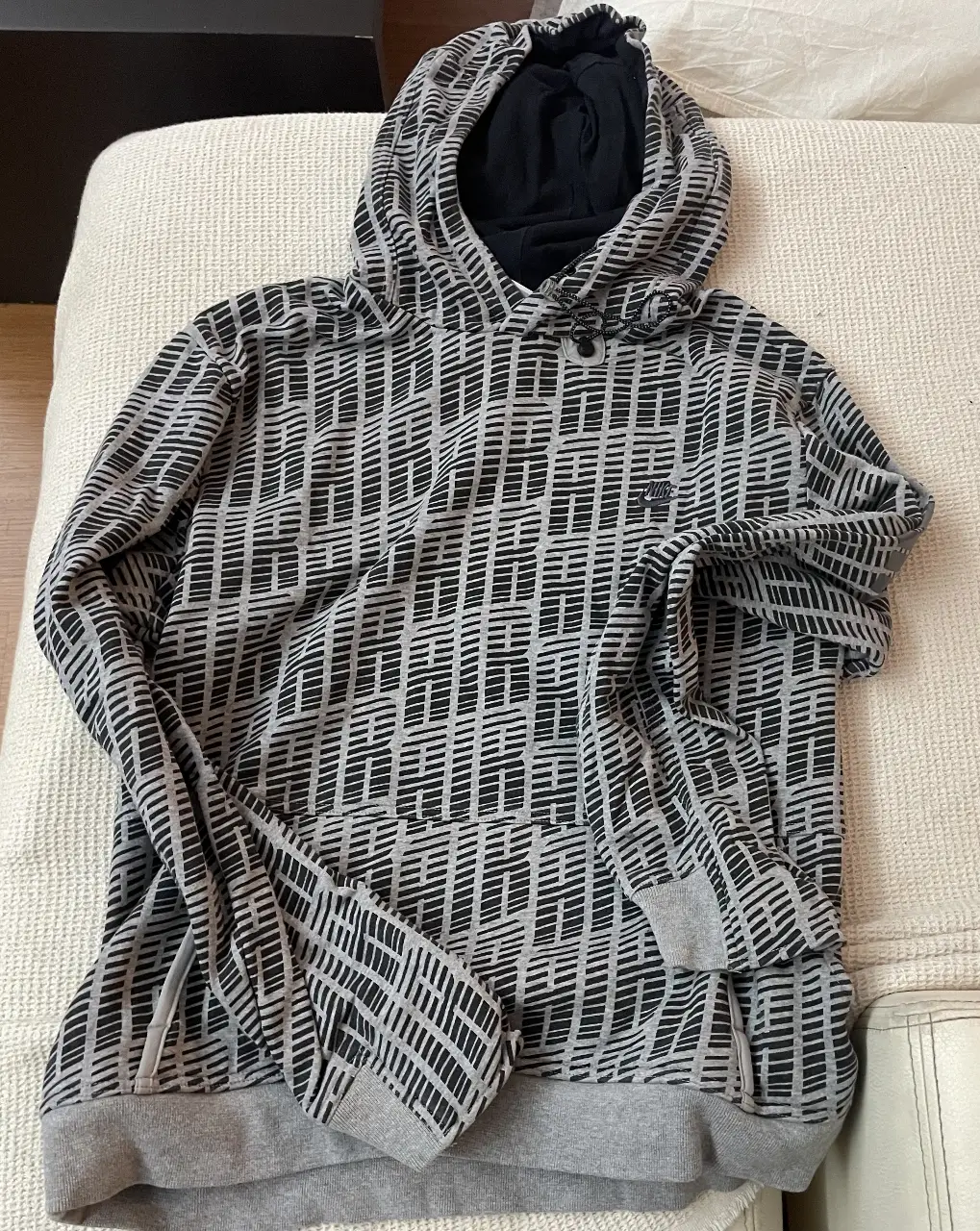 Buzo canguro Nike con capucha, estampado geométrico en tonos grises y negros. Ideal para un look deportivo y casual.