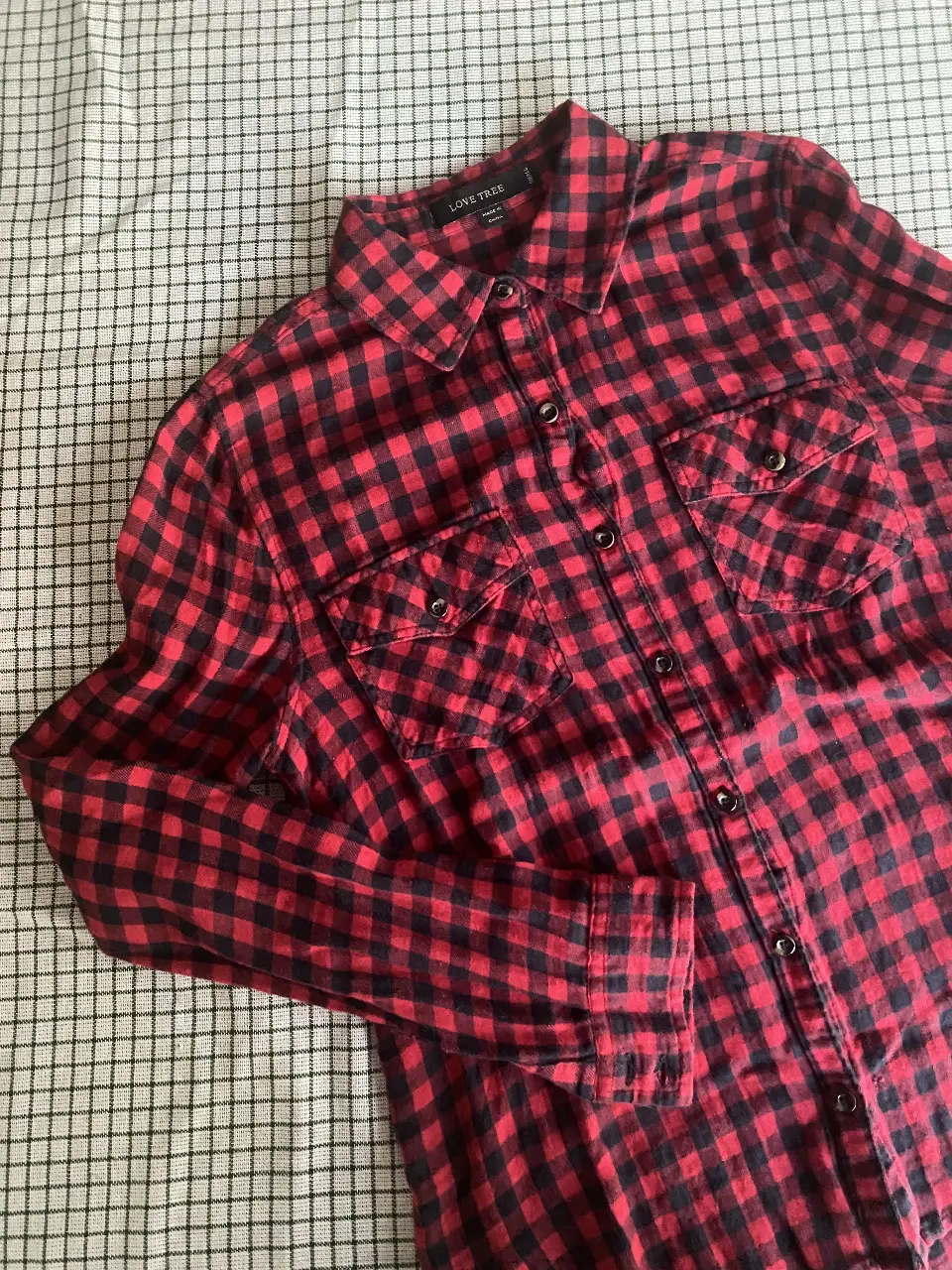 Camisa a cuadros roja y negra de manga larga, con dos bolsillos delanteros y cuello clásico. Ideal para un look casual y moderno.