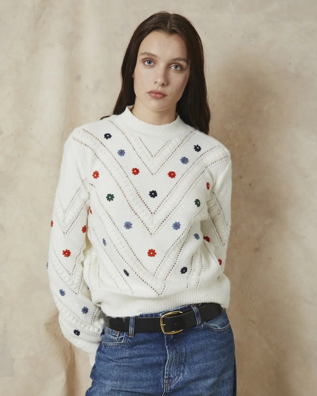 Sweater blanco de lana con cuello redondo y mangas largas. Posee un delicado bordado de flores en varios colores (rojo, azul, verde) distribuidas en el frente y las mangas. El diseño del tejido presenta un patrón en V en el frente y detalles de ochos en las mangas. Ideal para un look casual y tierno.