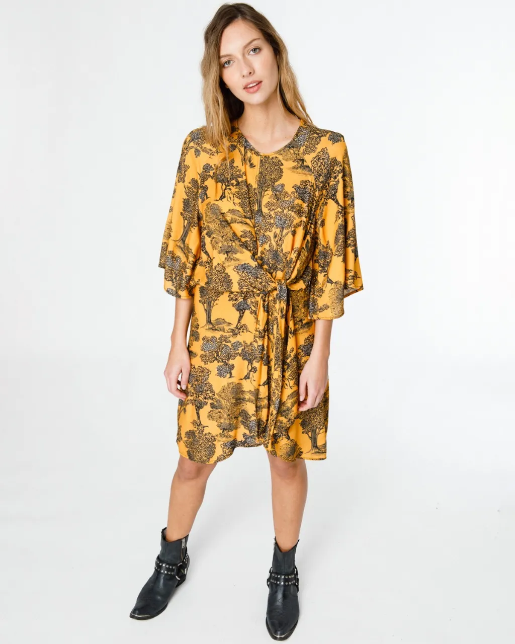 Vestido amarillo vibrante con estampa de árboles en negro. Diseño con nudo delantero y mangas amplias tipo mariposa. Ideal para un look boho chic o casual.