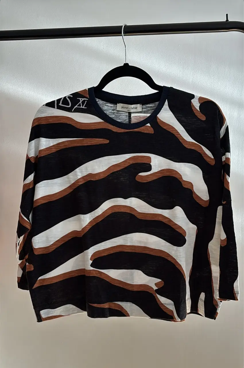 Remera de manga larga con estampado abstracto en blanco, negro y marrón. Cuello redondo con detalle en azul marino. Ideal para un look casual y moderno.